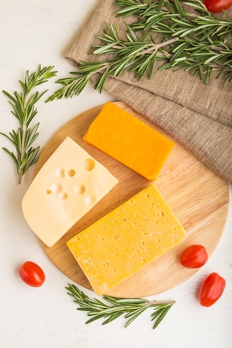 Various types of cheese with rosemary and tomatoes on wooden board on a white wooden background and linen textile. Top view, close up, flat lay, by ULADZIMIR ZGURSKI