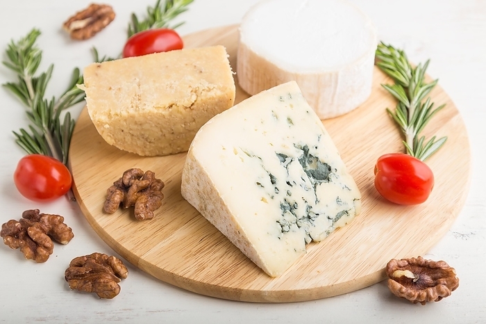 Blue cheese and various types of cheese with rosemary and tomatoes on wooden board on a white wooden background. Side view, close up, selective focus, by ULADZIMIR ZGURSKI