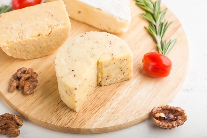 Cheddar and various types of cheese with rosemary and tomatoes on wooden board on a white wooden background. Side view, close up, selective focus, by ULADZIMIR ZGURSKI
