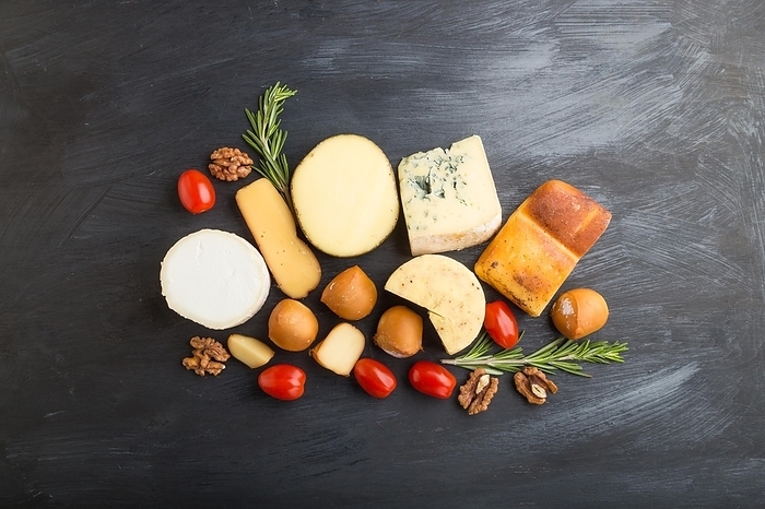 Set of different types of cheese with rosemary and tomatoes on a black wooden background. Top view, flat lay, copy space, by ULADZIMIR ZGURSKI
