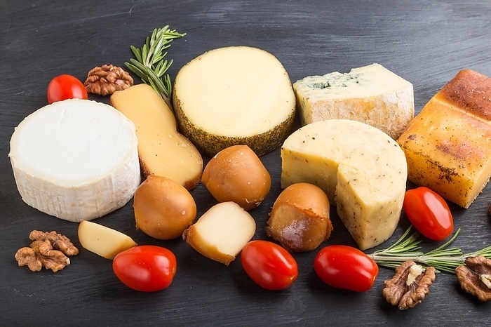 Set of different types of cheese with rosemary and tomatoes on a black wooden background. Side view, close up, by ULADZIMIR ZGURSKI