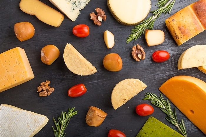 Set of different types of cheese with rosemary and tomatoes on a black wooden background. Top view, flat lay, close up, by ULADZIMIR ZGURSKI