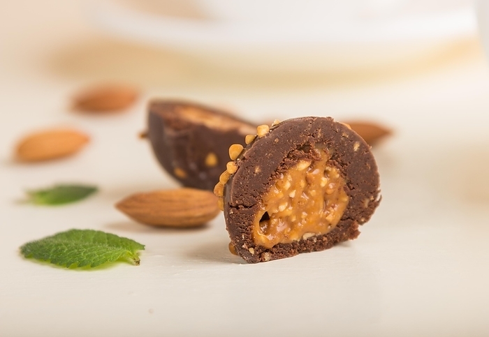 Chocolate caramel ball candies with almonds on a white wooden background. Side view, close up, selective focus, by ULADZIMIR ZGURSKI