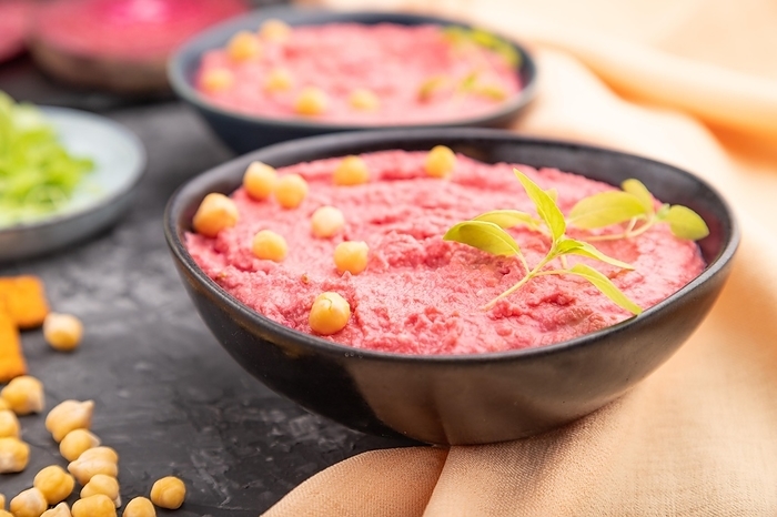 Hummus with beet and microgreen basil sprouts in ceramic bowl on a black concrete background and orange textile. Side view, close up, selective focus, by ULADZIMIR ZGURSKI