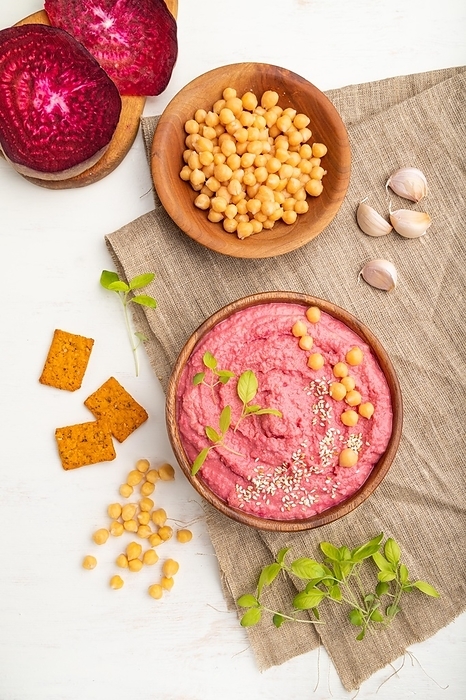 Hummus with beet and microgreen basil sprouts in wooden bowl on a white wooden background and linen textile. Top view, flat lay, close up, by ULADZIMIR ZGURSKI