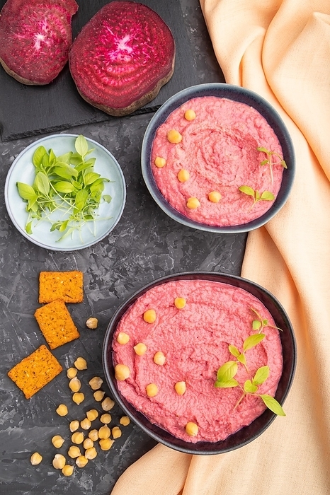 Hummus with beet and microgreen basil sprouts in ceramic bowl on a black concrete background and orange textile. Top view, flat lay, close up, by ULADZIMIR ZGURSKI