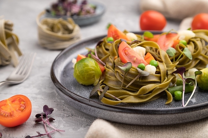 Tagliatelle green spinach pasta with tomato, pea and microgreen sprouts on a gray concrete background and linen textile. Side view, close up, selective focus, by ULADZIMIR ZGURSKI