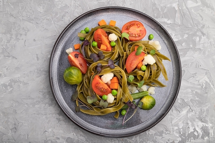 Tagliatelle green spinach pasta with tomato, pea and microgreen sprouts on a gray concrete background. Top view, flat lay, close up, by ULADZIMIR ZGURSKI