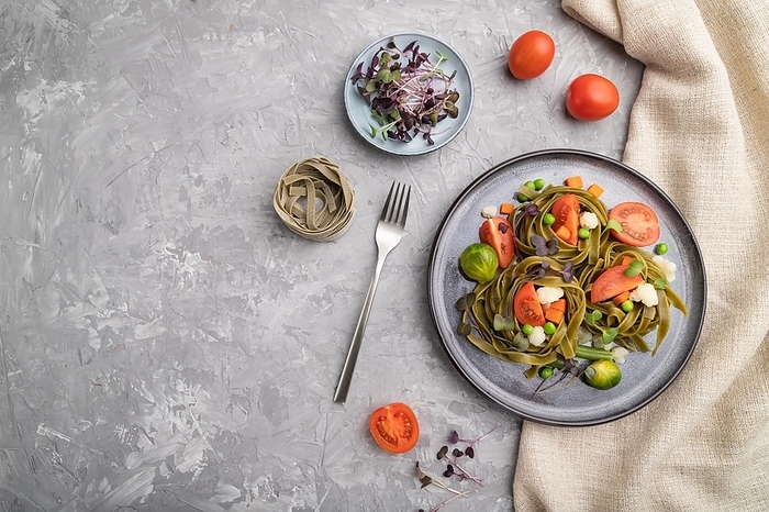 Tagliatelle green spinach pasta with tomato, pea and microgreen sprouts on a gray concrete background and linen textile. Top view, flat lay, copy space, by ULADZIMIR ZGURSKI