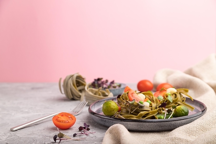 Tagliatelle green spinach pasta with tomato, pea and microgreen sprouts on a gray and pink background and linen textile. Side view, copy space, selective focus, by ULADZIMIR ZGURSKI