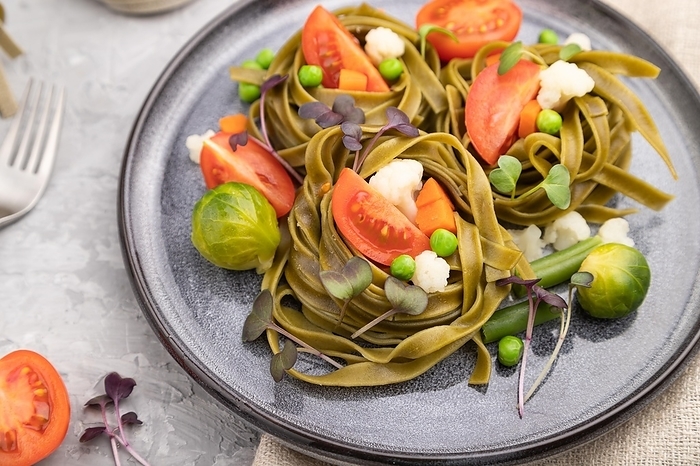 Tagliatelle green spinach pasta with tomato, pea and microgreen sprouts on a gray concrete background and linen textile. Side view, close up, selective focus, by ULADZIMIR ZGURSKI