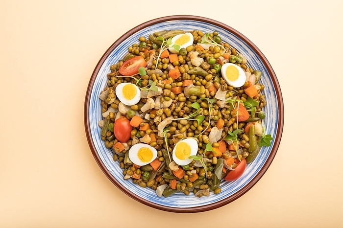 Mung bean porridge with quail eggs, tomatoes and microgreen sprouts on a pastel orange background. Top view, close up, by ULADZIMIR ZGURSKI