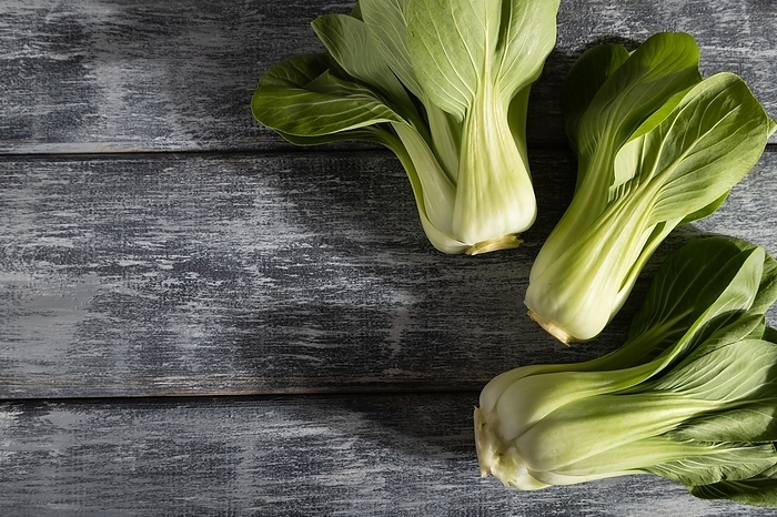 Fresh green bok choy or pac choi chinese cabbage on a gray wooden background. Hard light, contrast. Top view, copy space, flat lay, by ULADZIMIR ZGURSKI
