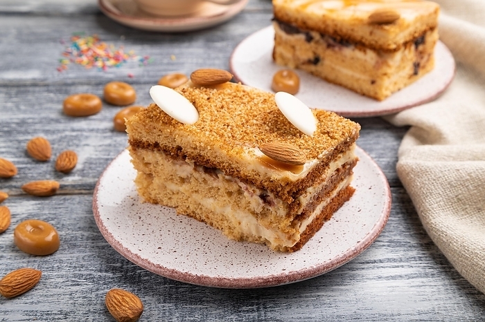 Honey cake with milk cream, caramel, almonds and a cup of coffee on a gray wooden background and linen textile. Side view, close up, by ULADZIMIR ZGURSKI