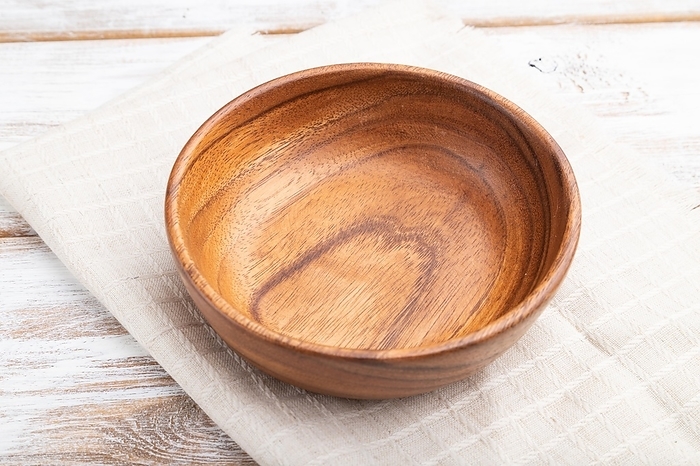 Empty wooden bowl on white wooden background and linen textile. Side view, close up, by ULADZIMIR ZGURSKI