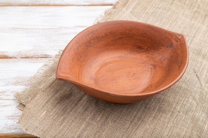 Empty clay brown bowl on white wooden background and linen textile. Side view, close up, by ULADZIMIR ZGURSKI