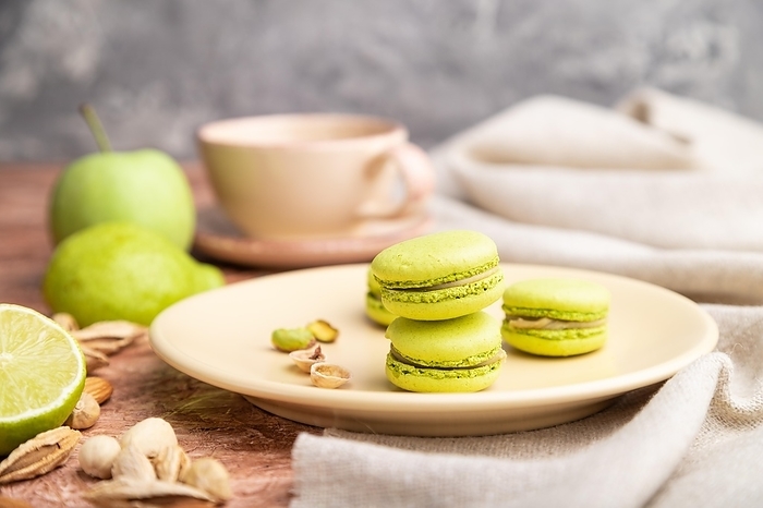 Green macarons or macaroons cakes with cup of coffee on a brown concrete background and linen textile. Side view, close up, selective focus, by ULADZIMIR ZGURSKI