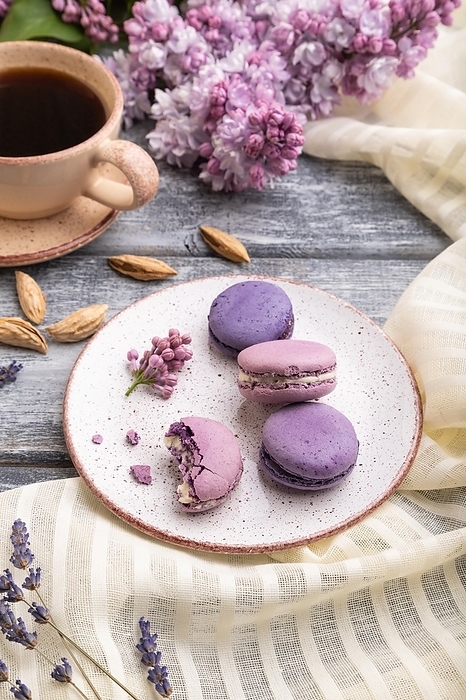 Purple macarons or macaroons cakes with cup of coffee on a gray wooden background and white linen textile. Side view, close up, by ULADZIMIR ZGURSKI