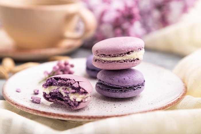Purple macarons or macaroons cakes with cup of coffee on a gray wooden background and white linen textile. Side view, close up, selective focus, by ULADZIMIR ZGURSKI