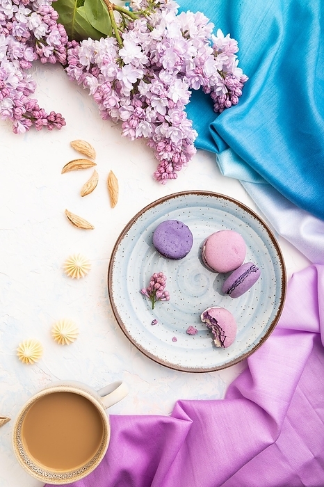 Purple macarons or macaroons cakes with cup of coffee on a white concrete background and magenta-blue textile. Top view, flat lay, close up, by ULADZIMIR ZGURSKI