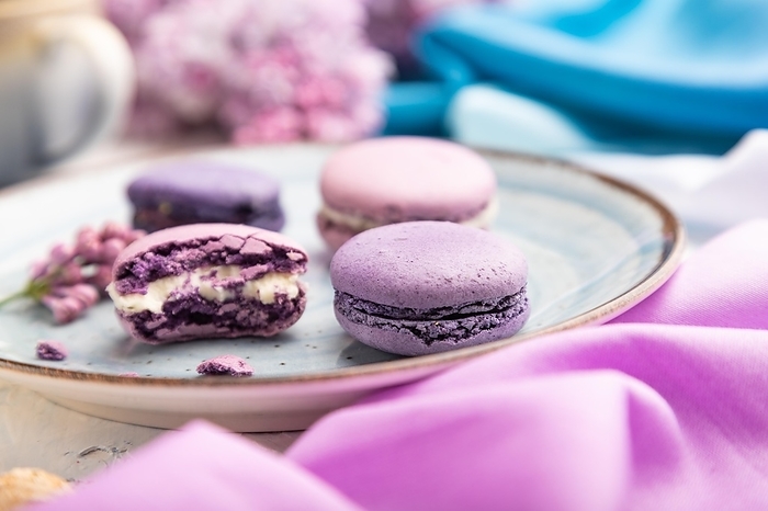Purple macarons or macaroons cakes with cup of coffee on a white concrete background and magenta-blue textile. Side view, close up, selective focus, by ULADZIMIR ZGURSKI