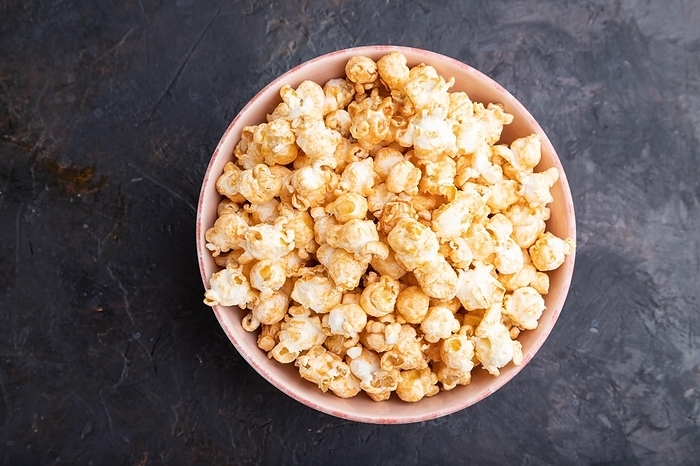 Popcorn with caramel in ceramic bowl on a black concrete background. Top view, flat lay, close up, by ULADZIMIR ZGURSKI