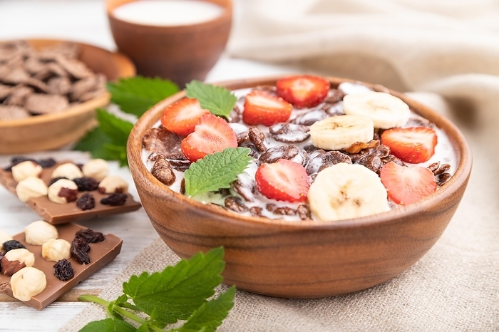 Chocolate cornflakes with milk and strawberry in wooden bowl on white wooden background and linen textile. Side view, close up, selective focus, by ULADZIMIR ZGURSKI