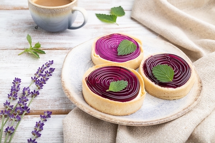 Sweet tartlets with jelly and milk cream with cup of coffee on a white wooden background and linen textile. Side view, close up, by ULADZIMIR ZGURSKI