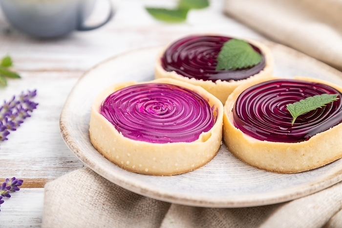 Sweet tartlets with jelly and milk cream with cup of coffee on a white wooden background and linen textile. Side view, close up, selective focus, by ULADZIMIR ZGURSKI