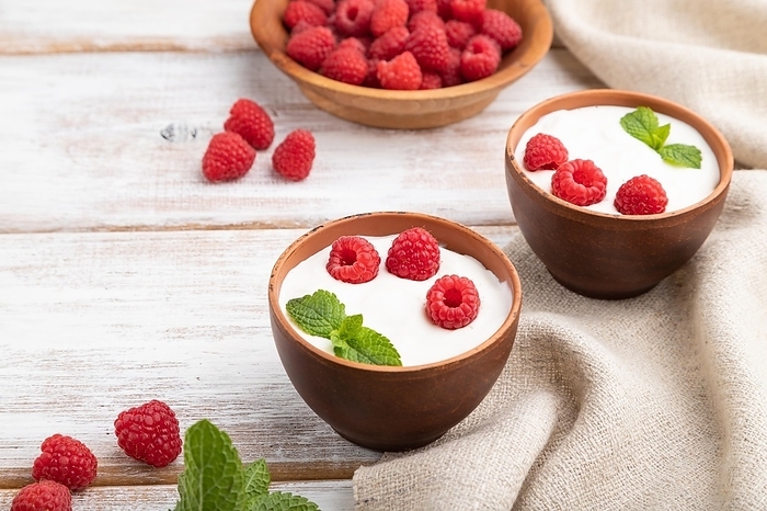 Yogurt with raspberry in clay cups on white wooden background and linen textile. Side view, close up, by ULADZIMIR ZGURSKI