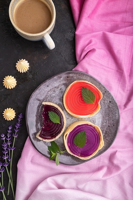 Sweet tartlets with jelly and milk cream with cup of coffee on a black concrete background and pink textile. top view, flat lay, close up, by ULADZIMIR ZGURSKI