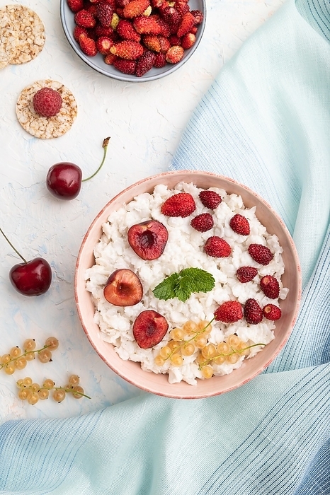 Rice flakes porridge with milk and strawberry in ceramic bowl on white concrete background and blue linen textile. Top view, flat lay, close up, by ULADZIMIR ZGURSKI
