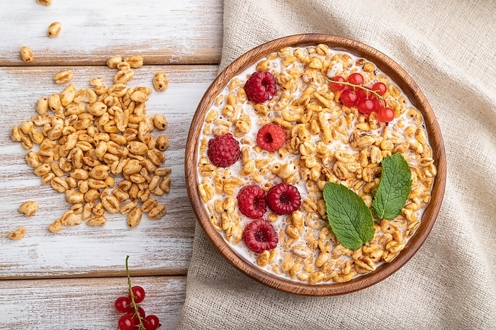 Wheat flakes porridge with milk, raspberry and currant in wooden bowl on white wooden background and linen textile. Top view, flat lay, close up, by ULADZIMIR ZGURSKI