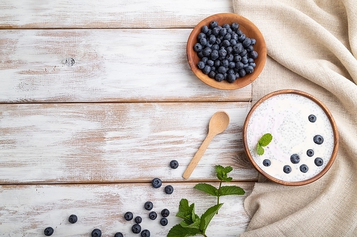 Yogurt with blueberry in wooden bowl on white wooden background and linen textile. top view, flat lay, copy space, by ULADZIMIR ZGURSKI