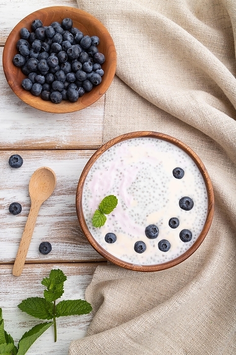 Yogurt with blueberry in wooden bowl on white wooden background and linen textile. top view, flat lay, close up, by ULADZIMIR ZGURSKI