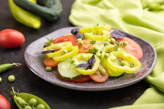 Vegetarian salad from green pea, tomatoes, pepper and basil on a black concrete background and green textile. Side view, close up, selective focus, by ULADZIMIR ZGURSKI