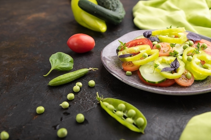 Vegetarian salad from green pea, tomatoes, pepper and basil on a black concrete background and green textile. Side view, close up, selective focus, by ULADZIMIR ZGURSKI