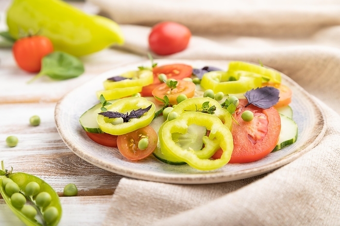 Vegetarian salad from green pea, tomatoes, pepper and basil on white wooden background and linen textile. Side view, close up, selective focus, by ULADZIMIR ZGURSKI