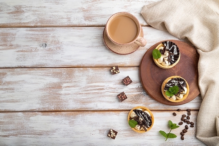 Sweet tartlets with chocolate and cheese cream with cup of coffee on a white wooden background and linen textile. top view, flat lay, copy space, by ULADZIMIR ZGURSKI