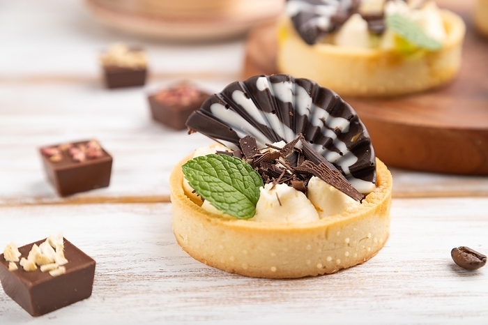 Sweet tartlets with chocolate and cheese cream with cup of coffee on a white wooden background and linen textile. side view, close up, selective focus, by ULADZIMIR ZGURSKI