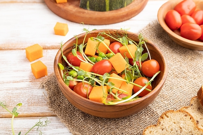 Vegetarian vegetable salad of tomatoes, pumpkin, microgreen pea sprouts on white wooden background and linen textile. Side view, close up, by ULADZIMIR ZGURSKI