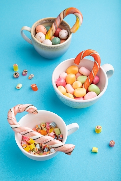 Heap of multicolored caramel candies in cups on blue pastel background. close up, side view, by ULADZIMIR ZGURSKI