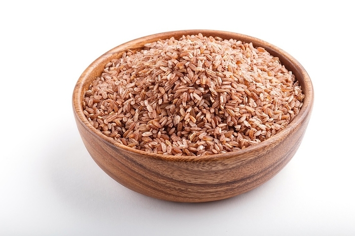 Wooden bowl with unpolished brown rice isolated on white background. Side view, close up, by ULADZIMIR ZGURSKI