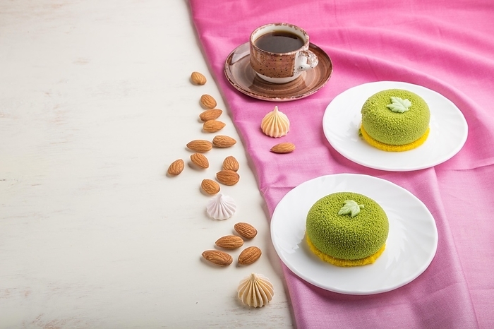Green mousse cake with pistachio cream and a cup of coffee on a white wooden background and pink textile. side view, copy space, by ULADZIMIR ZGURSKI