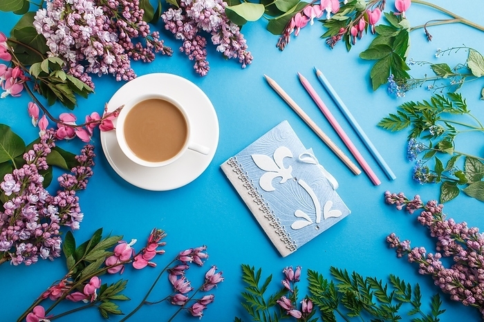 Purple lilac and bleeding heart flowers and a cup of coffee with notebook and colored pencils on pastel blue background. Morninig, spring, fashion composition. Flat lay, top view, by ULADZIMIR ZGURSKI