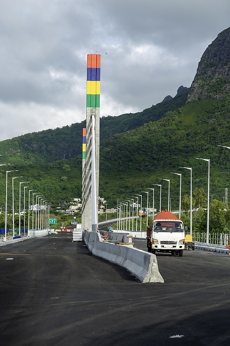 Mauritius A highway with Mauritian emblem on pillar and a truck driving, surrounded by mountains and an overcast sky.A1 M1 Link Bridge At Grand River North West Valley on the island of Mauritius, by Doukdouk