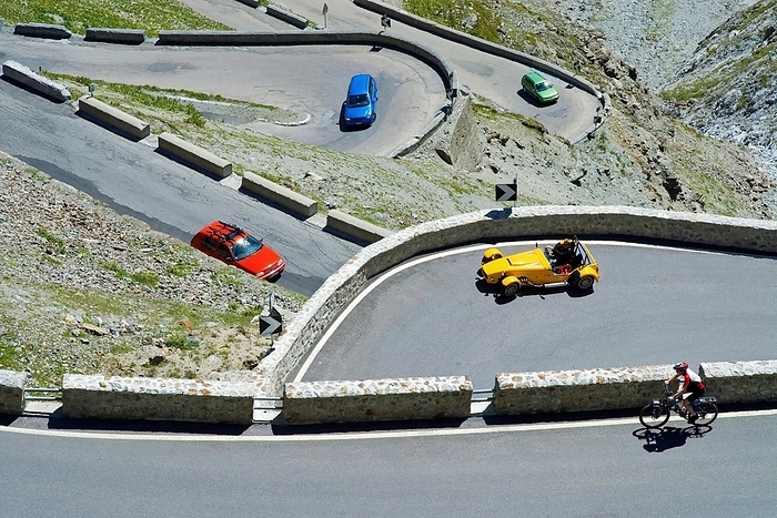 Italy A red, green and blue car, a yellow roadster and a bicycle driver in hairpin curves on the Stelvio Pass, South Tyrol, Italy, Europe, by Dirk v. Mallinckrodt