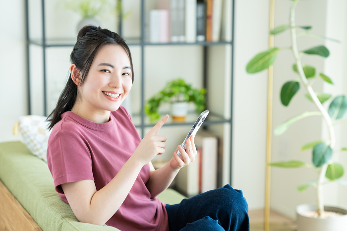 Young Japanese woman looking at her phone in her living room.