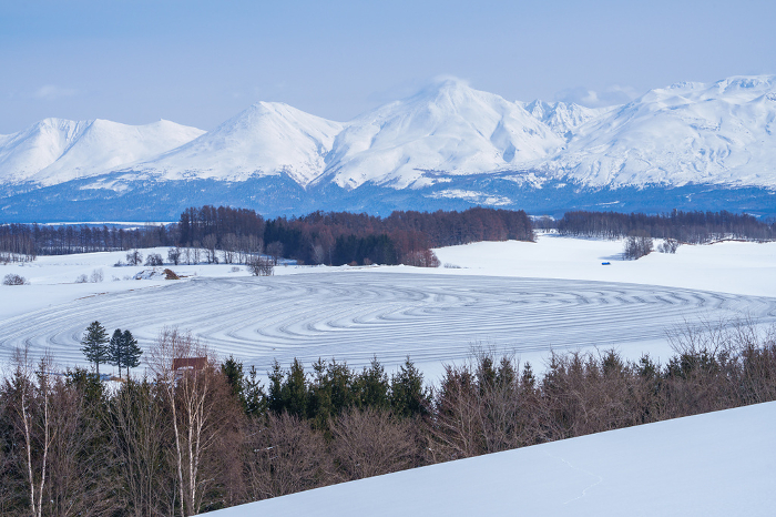 Shin-ei Hill in Biei in late winter. Snow field sprinkled with snow-melting agent and the Tokachi Mountain Range