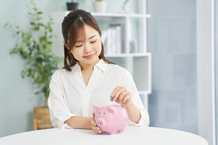 Japanese woman putting money into piggy bank (People)